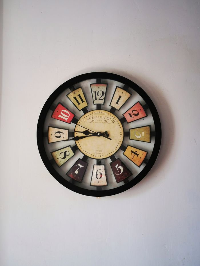 A retro-style wooden wall clock with colorful numbers in a minimalist room setting.