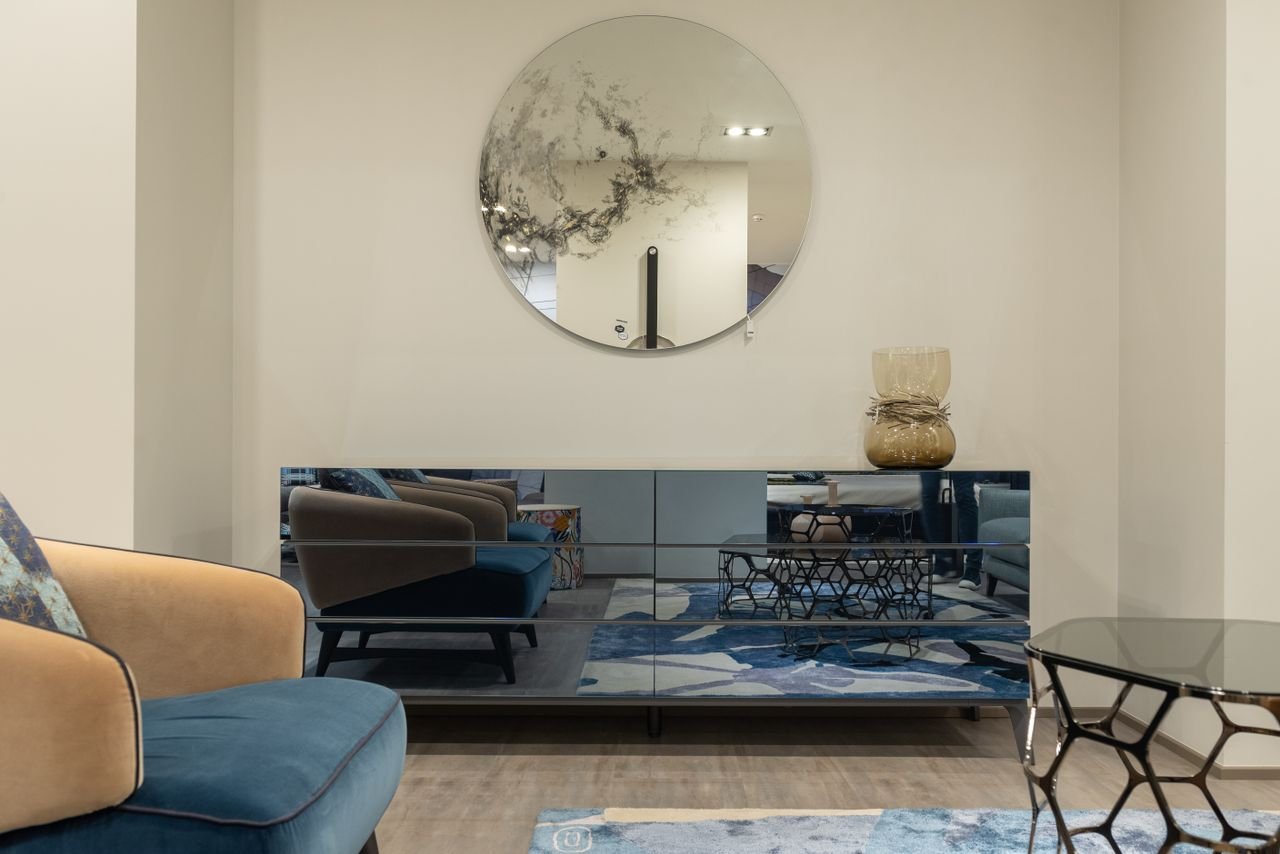 Modern interior of luxury living room with comfortable armchair and shining table against mirror on wall and glowing dresser